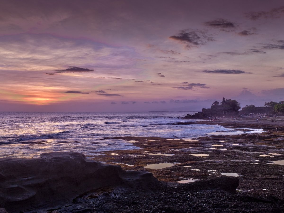 The sea temple of Tanah Lot silhouetted against a sunset over the Bali coast