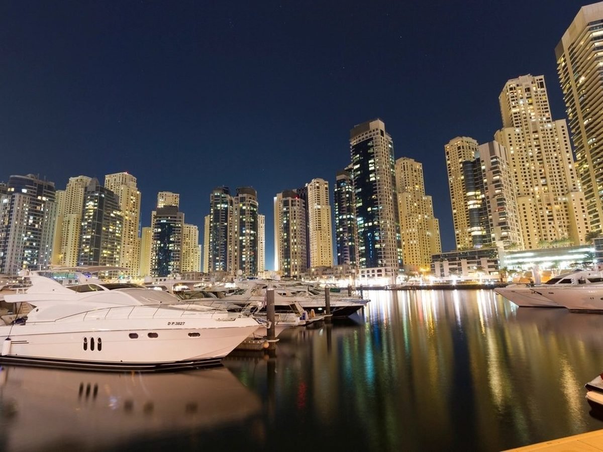 Yachts moored along Dubai Marina with lit towers rising behind them at dusk