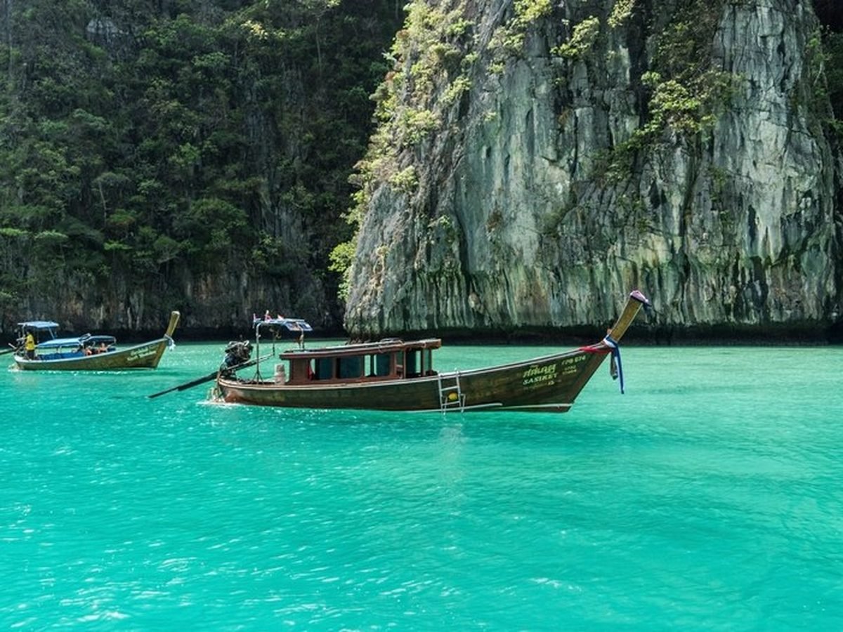 Longtail boats moored in the turquoise water of a limestone bay in Thailand